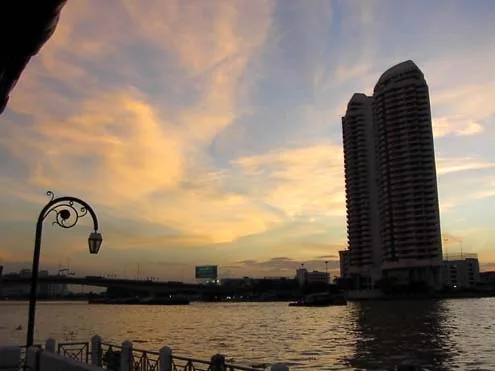 Chao Phraya River at dusk with boats, city skyline and a riverside lamp