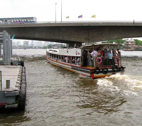 Chao Phraya river bus crowded with passengers passing under a Bangkok bridge