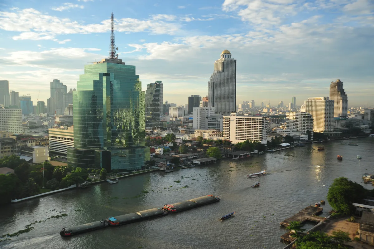 Chao Phraya River panorama with boats and Bangkok skyscrapers in golden light