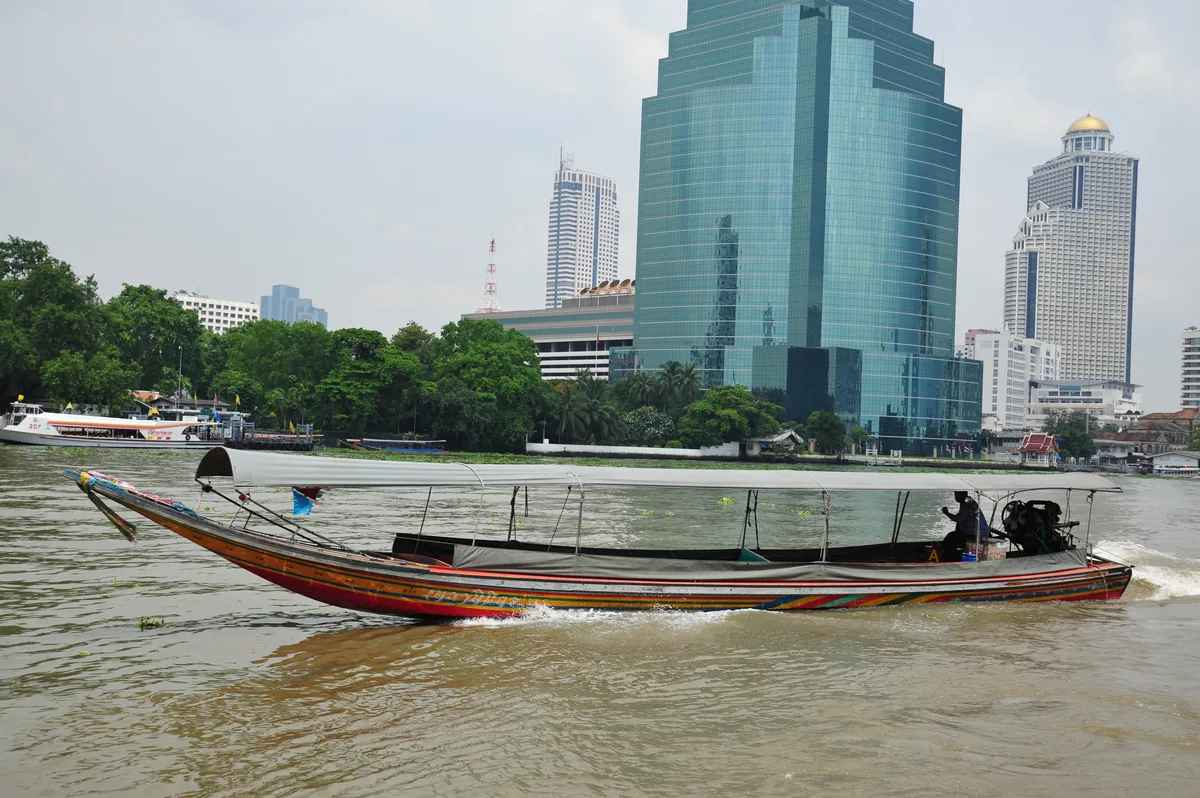 Traditional long-tail boat on the Chao Phraya River with the Bangkok skyline behind