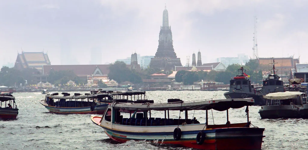 Long-tail boats and ferries on the Chao Phraya River with Wat Arun temple behind